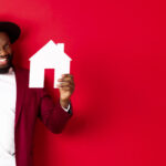 millennial black man holding white home in red background